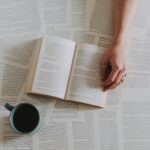 A peaceful setup with an open book and coffee cup surrounded by scattered pages.